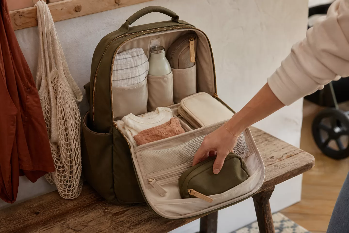 An open olive diaper backpack organized with a change of clothes, cloth, bottle, and small pouches